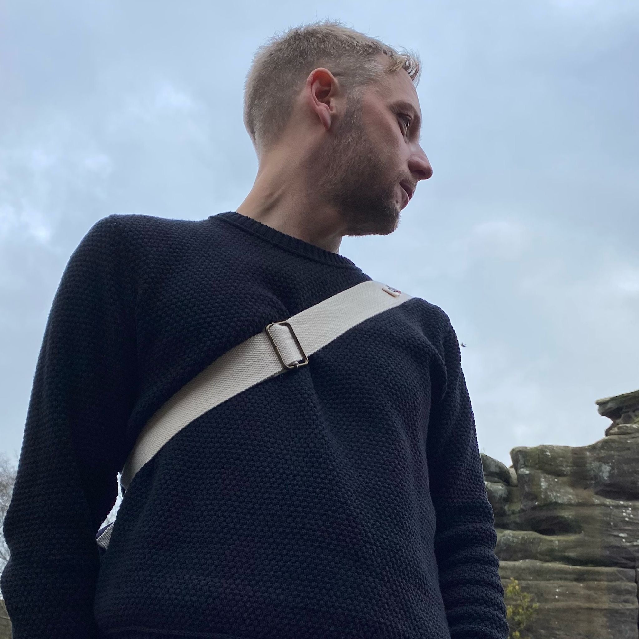 A man looking out at the rocky scenery wearing our Eco-Knit Jumper in Navy and our Ditty Bag on his back. 